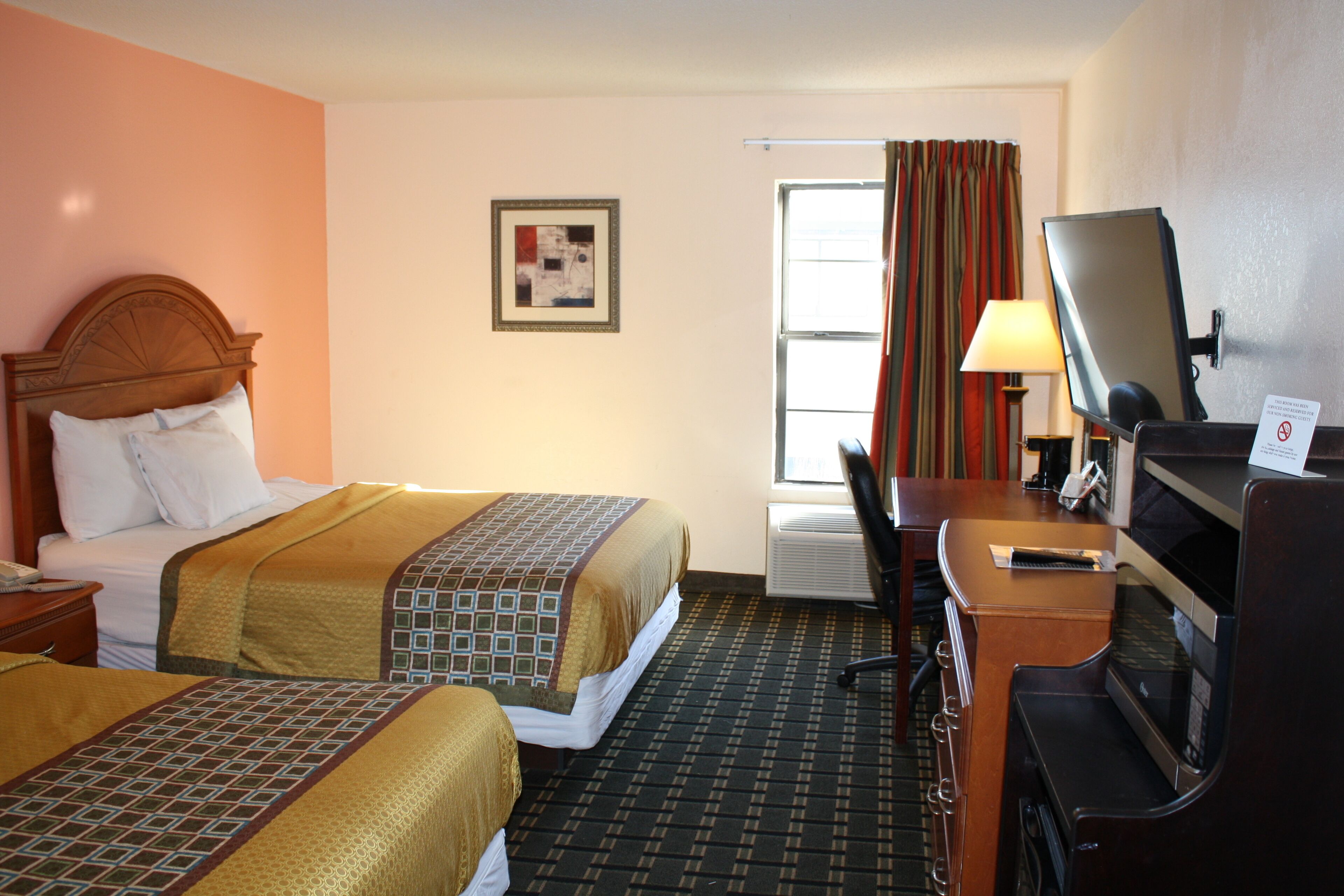 A hotel room with two beds, a desk with a computer, a TV, and a window with curtains.