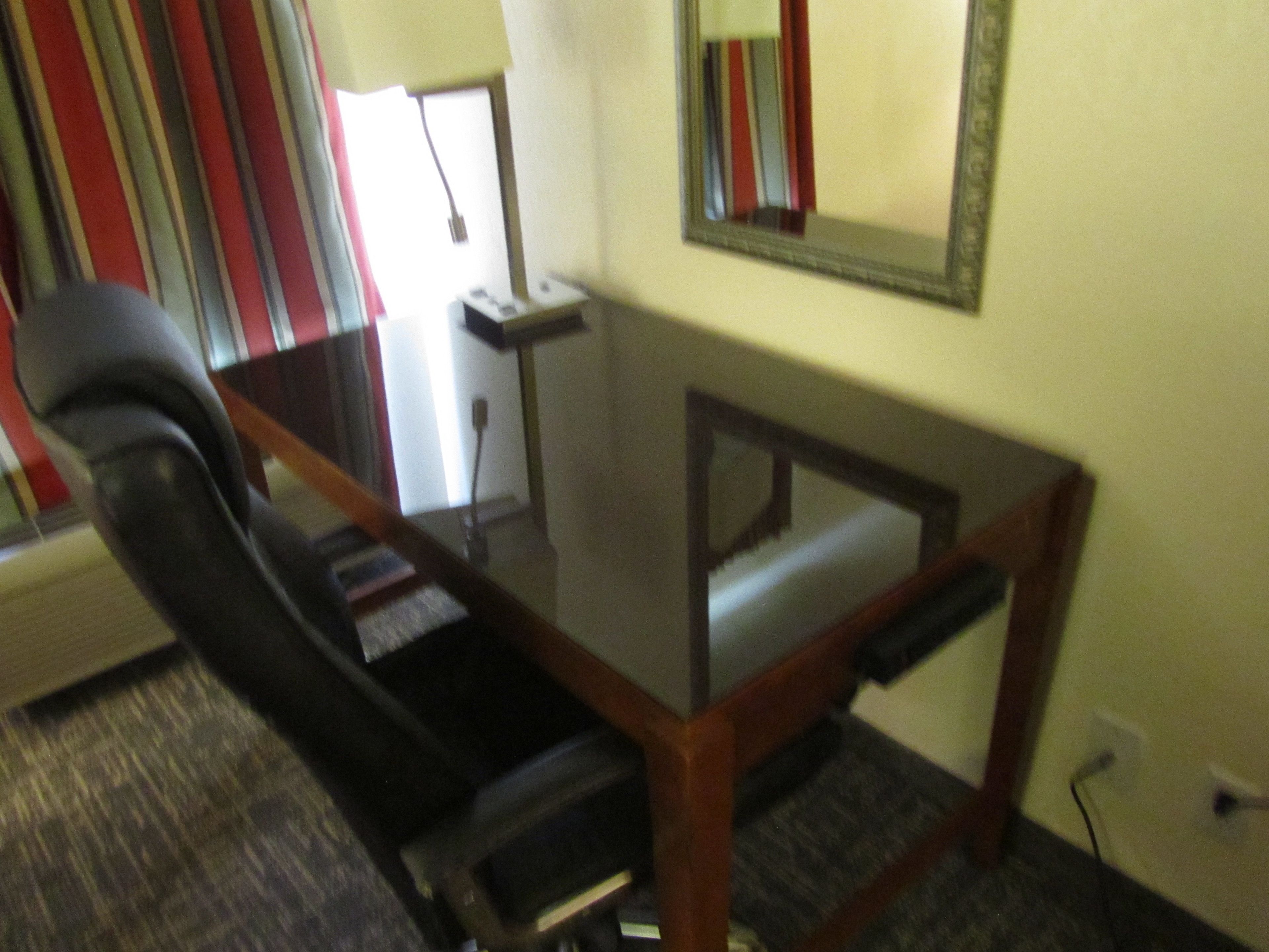 A conference room with a glass table, a black office chair, a small side table, and a mirror on the wall.