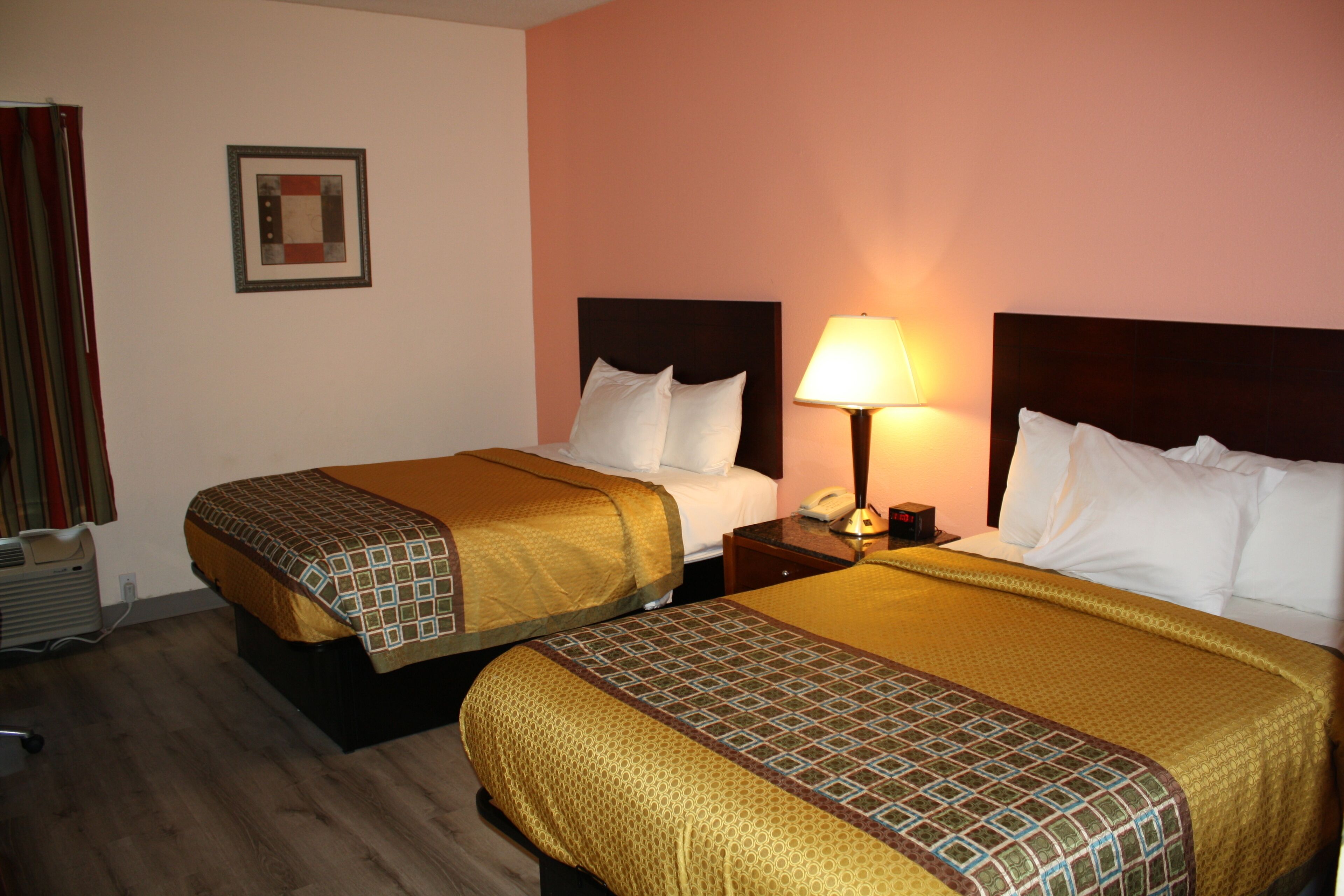 A hotel room with two beds, each with a patterned bedspread, a bedside table with a lamp, and a framed picture on the wall.
