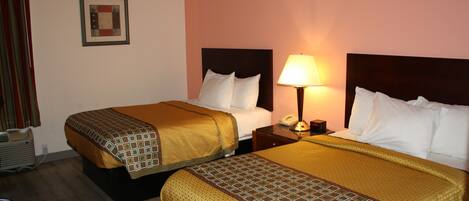 A hotel room with two beds, each with a patterned bedspread, a bedside table with a lamp, and a framed picture on the wall.