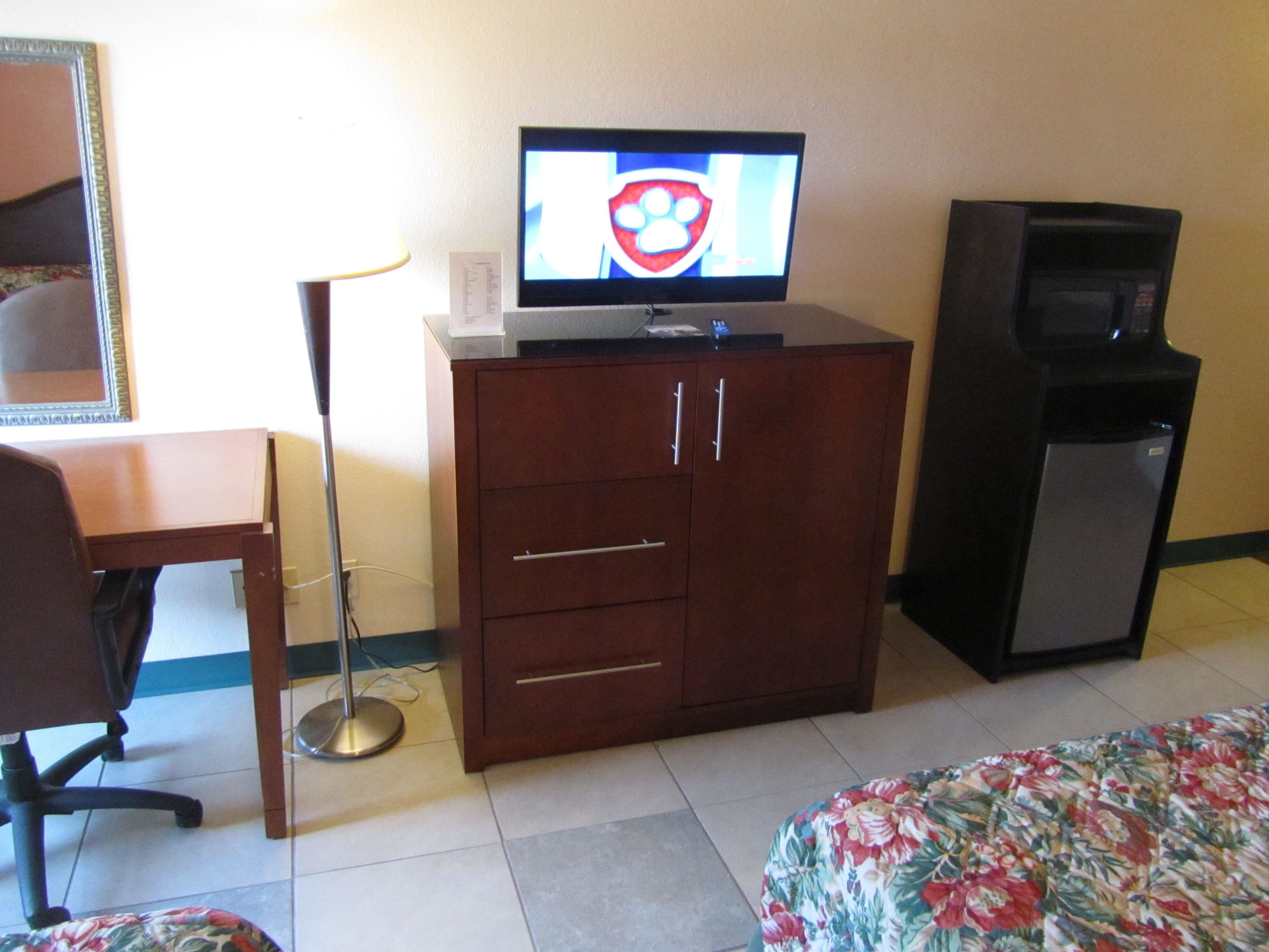 A hotel room with a wooden cabinet, a television on top, a small refrigerator, a desk, and a chair.