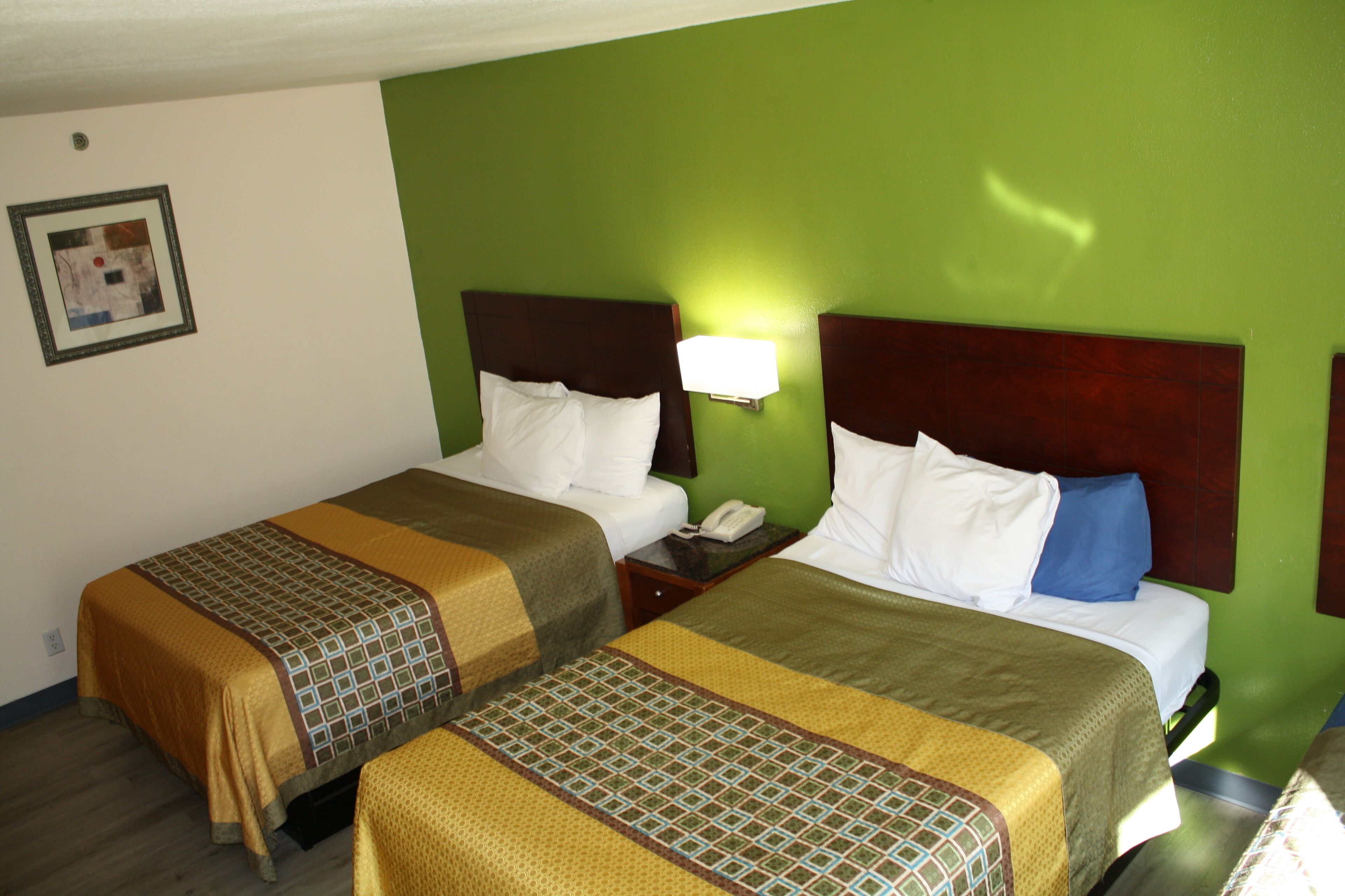 Habitación de hotel con dos camas, paredes verdes y un cuadro en la pared.