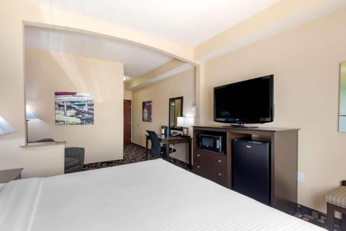 A hotel room with a bed, a desk with a computer, a television, and a refrigerator.