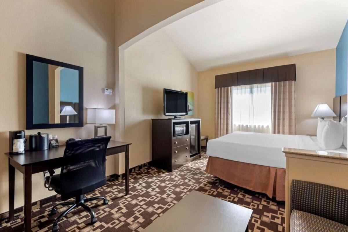 Une chambre d’hôtel équipée d’un lit, d’un bureau, d’une chaise, d’une télévision et d’une fenêtre avec des rideaux.
