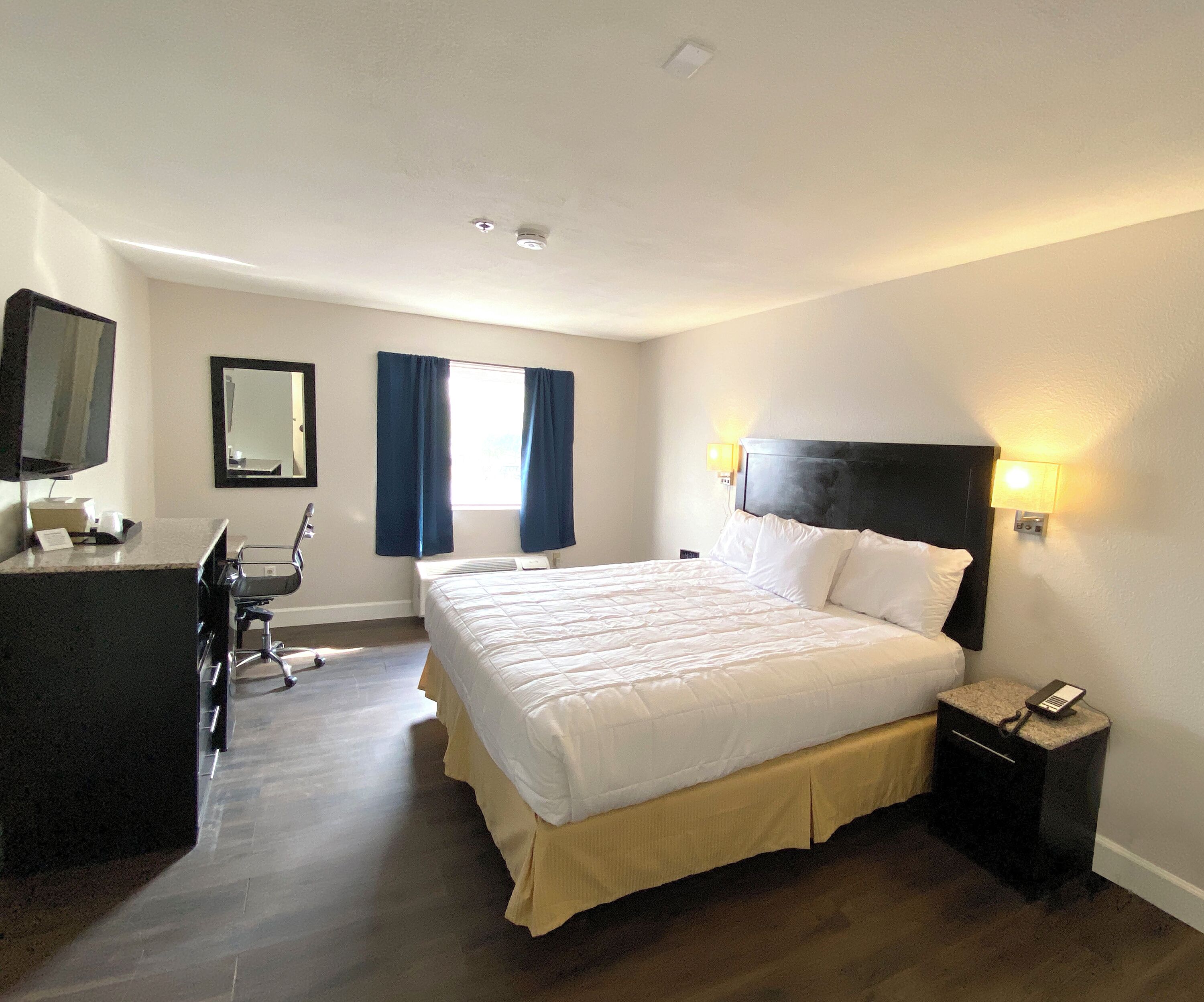 A hotel room with a bed, desk, chair, and a mirror.