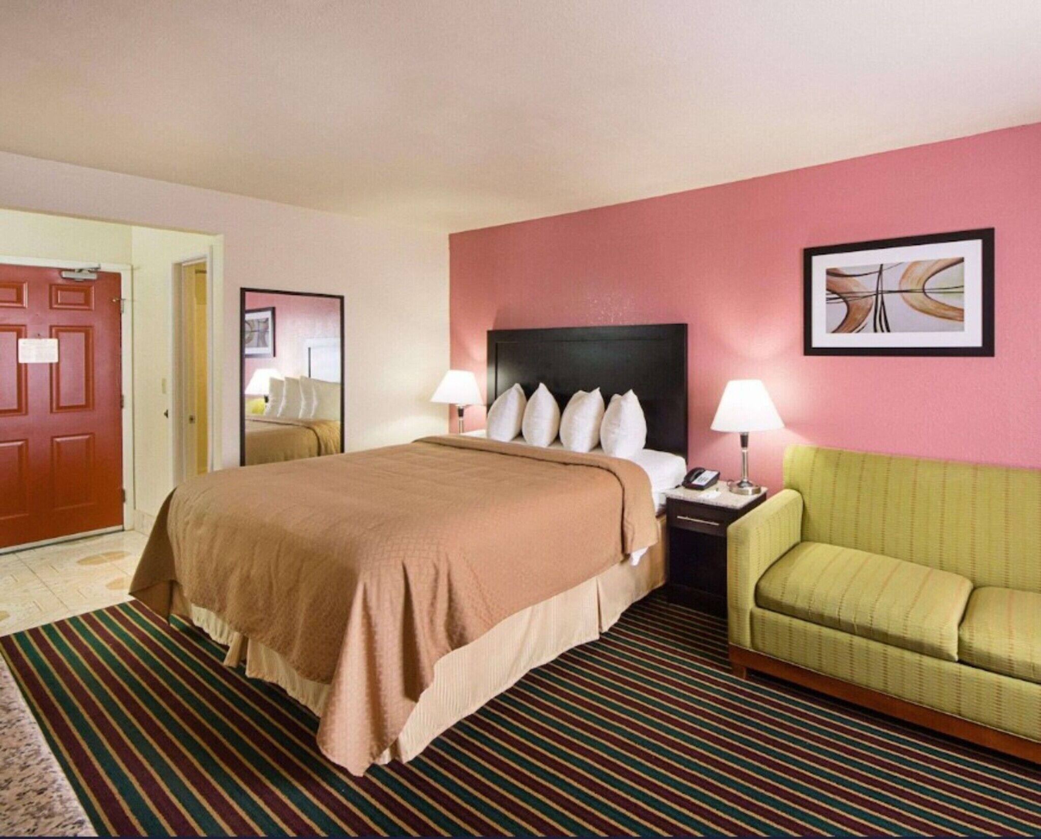 A hotel room with a bed, bedside tables, a green armchair, a door, and a framed picture on the wall.