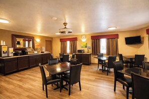A hotel room with a kitchenette, dining area with tables and chairs, a clock on the wall, and a TV mounted on the wall. - Quality Inn Del Rio (Del Rio)