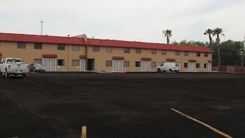 A motel with a red roof and beige walls, featuring a parking lot with several vehicles.