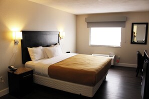 A hotel room with a bed, bedside lamps, a nightstand with a phone, a window with a view, and a mirror on the wall. - Quality Inn Del Rio (Del Rio)