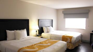 A hotel room with two beds, a nightstand, a lamp, and a window with a view.
