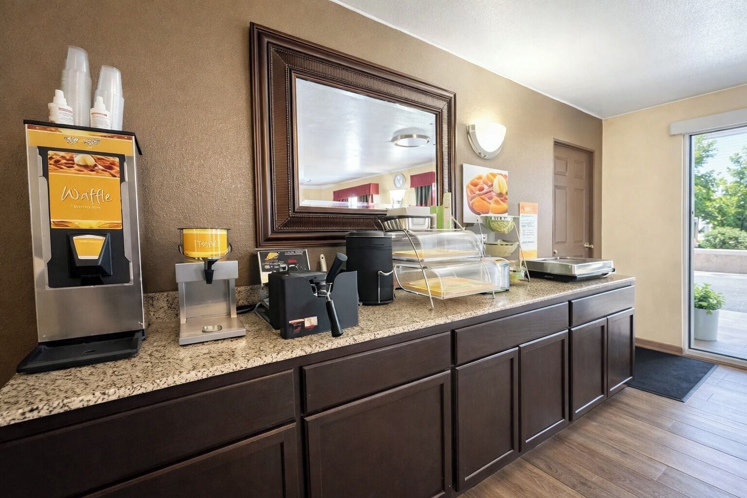 Una barra de cocina de hotel con una máquina para gofres, una cafetera y una exposición de fruta.