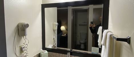 A bathroom with a granite countertop, a sink, a mirror, and a hairdryer.