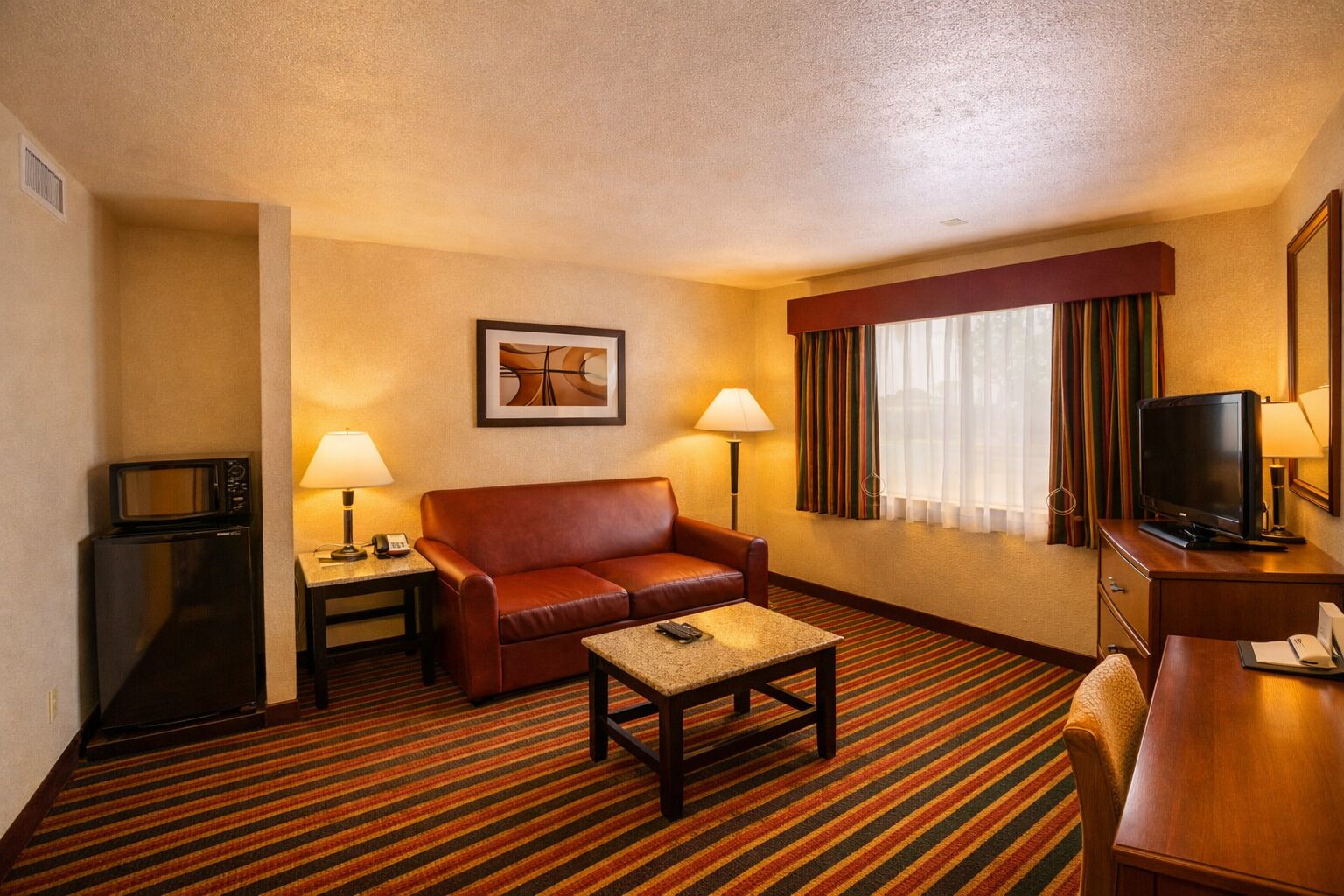 A hotel room with a sofa, a coffee table, a television, a microwave, and a lamp.