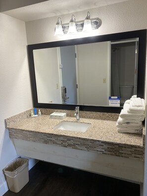 A bathroom with a granite countertop, a sink, a mirror, and a towel rack. - Quality Inn Del Rio (Del Rio)