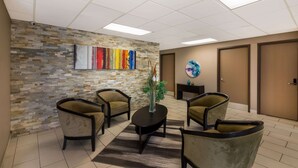 A modern waiting area with a stone wall, a colorful abstract painting, a round table with a vase, and four armchairs. - Quality Inn & Suites Round Rock - Austin North (Round Rock)