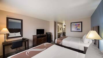 A hotel room with two beds, a desk with a chair, a television, and a mirror.