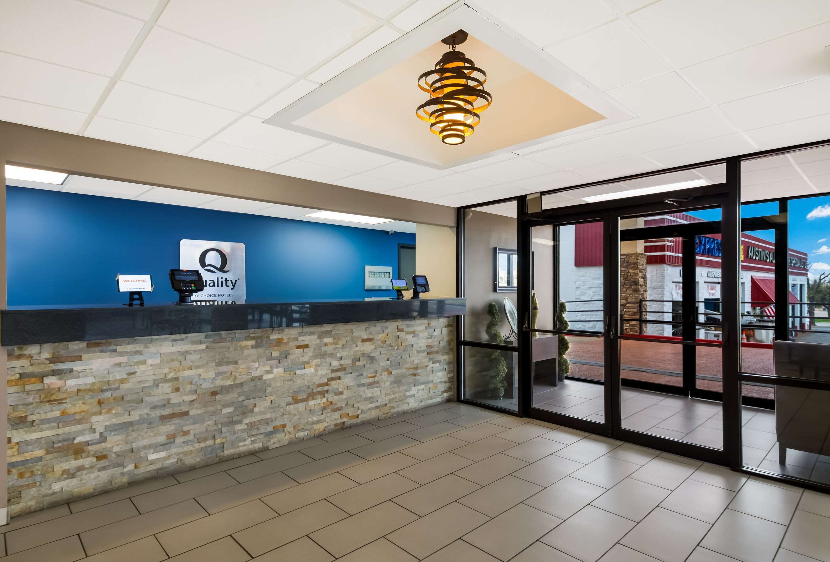 A hotel reception area with a blue wall, a stone accent wall, a reception desk, a modern chandelier, and large glass doors leading to an outdoor patio.