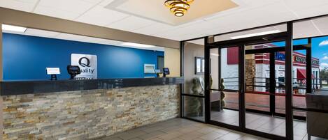 A hotel reception area with a blue wall, a stone accent wall, a reception desk, a modern chandelier, and large glass doors leading to an outdoor patio.