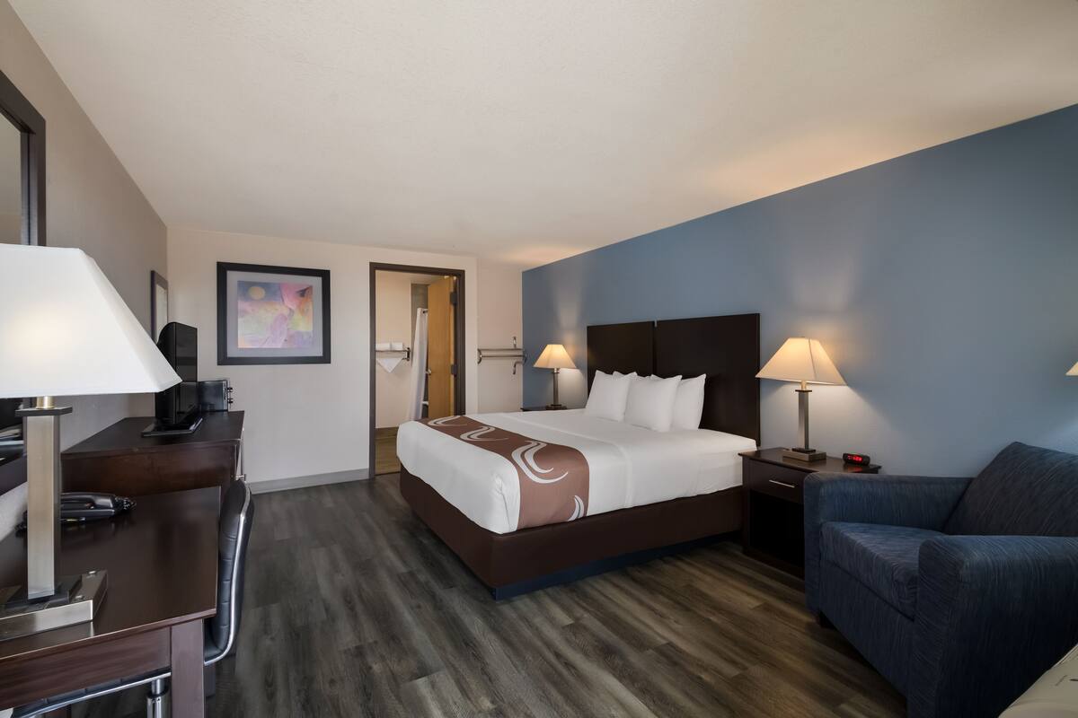 A hotel room with a bed, desk, chair, and a couch.