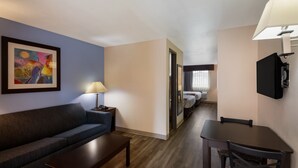 A hotel room with a sofa, a small table, a TV, a lamp, and a bed in the background. - Quality Inn & Suites Round Rock - Austin North (Round Rock)