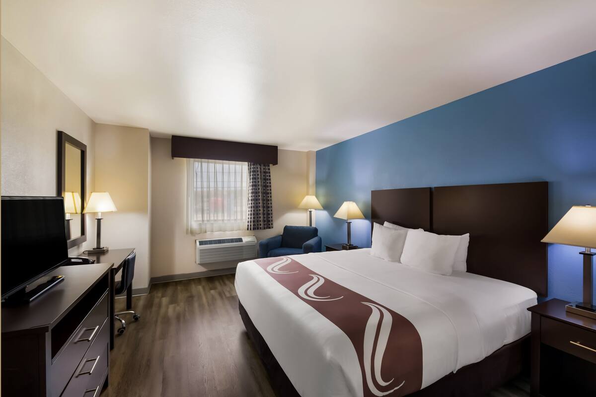 A hotel room with a large bed, a desk with a computer, a TV, and two lamps.