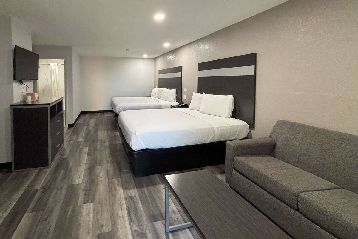 A hotel room with two beds, a sofa, a TV, and a small table.