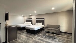 Une chambre d’hôtel avec deux lits, un canapé, une petite table et un téléviseur fixé au mur.