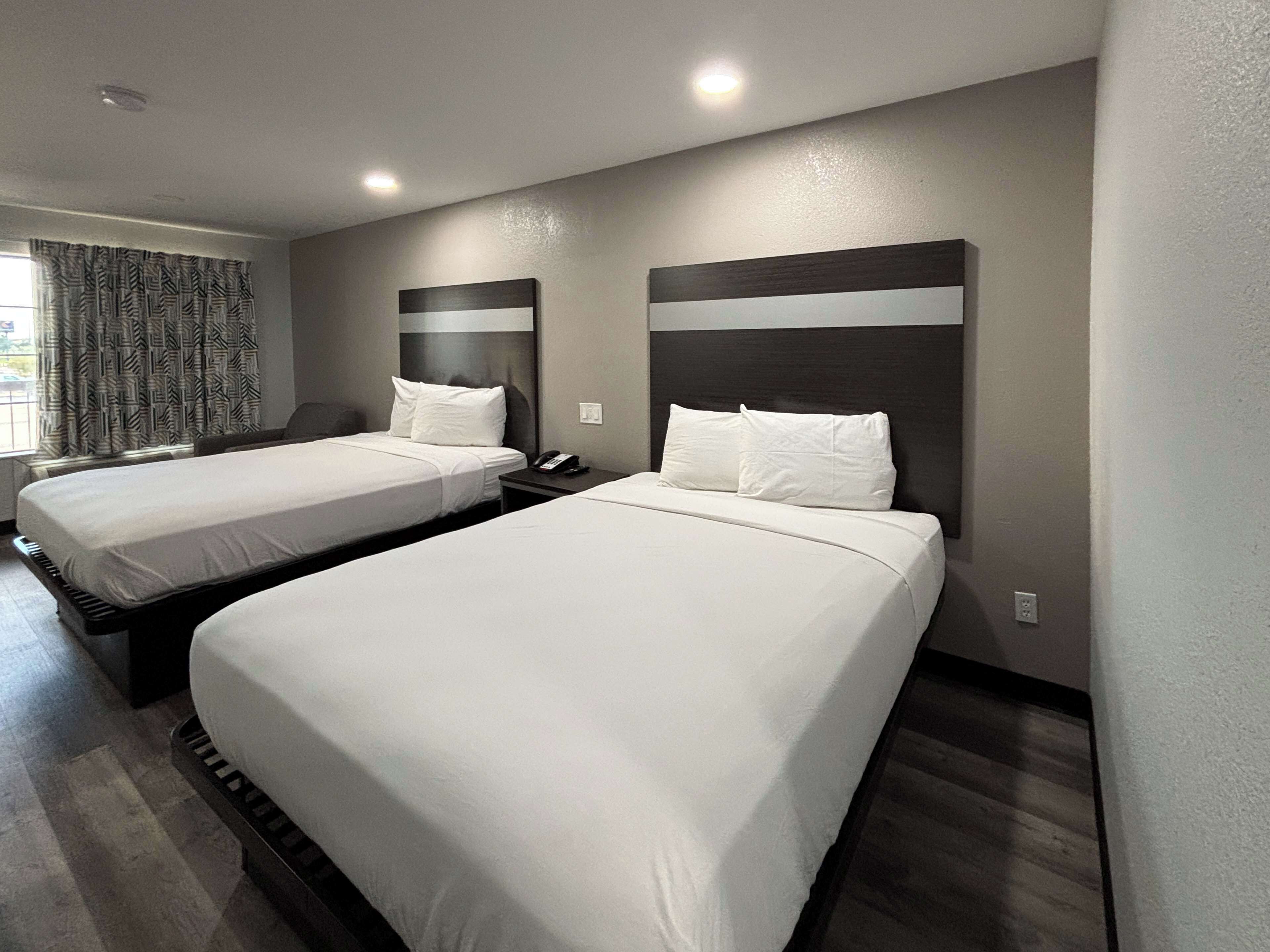 A hotel room with two beds, a telephone, and a window with curtains.