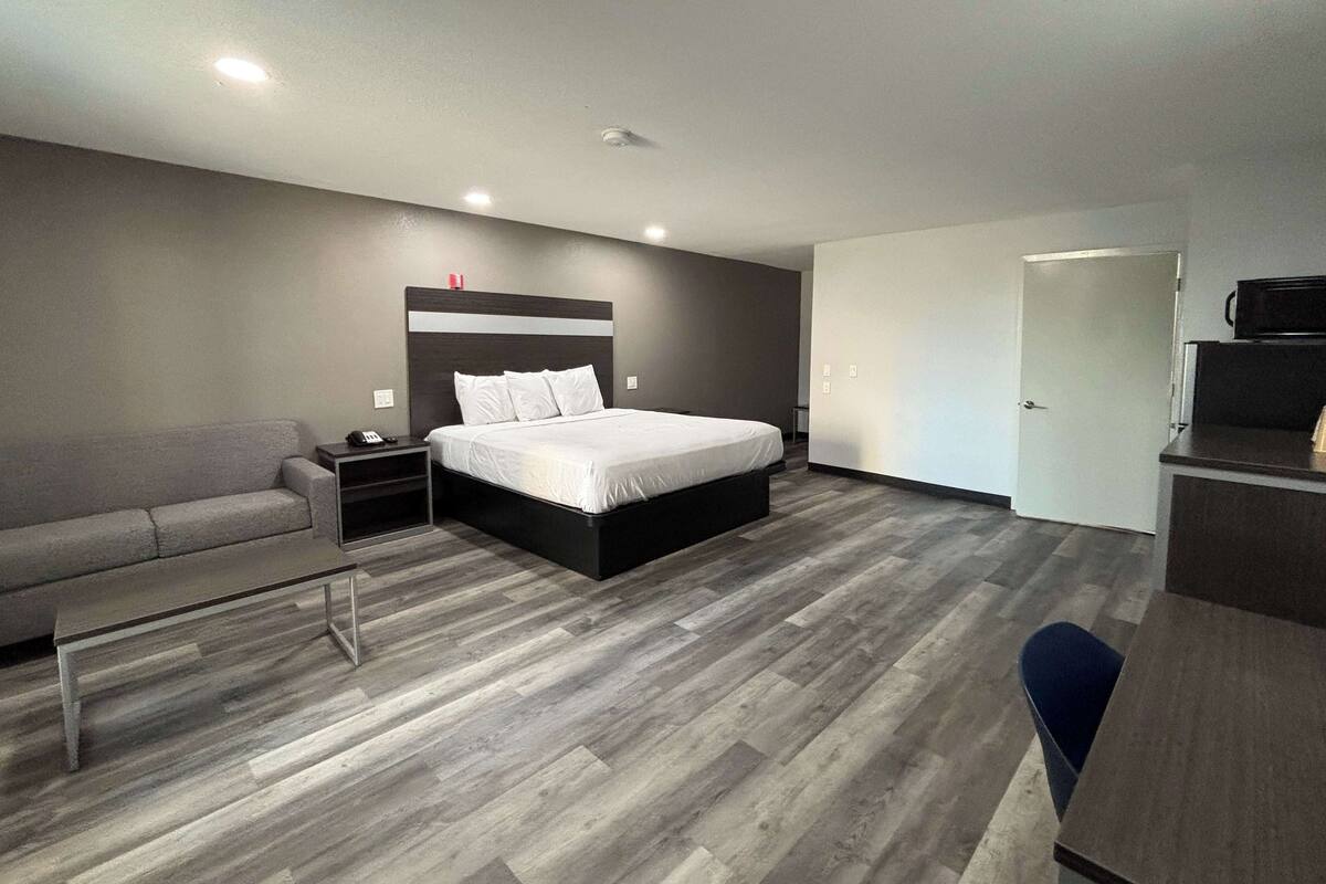 A modern hotel room with a large bed, a sofa, a desk, and a wardrobe.