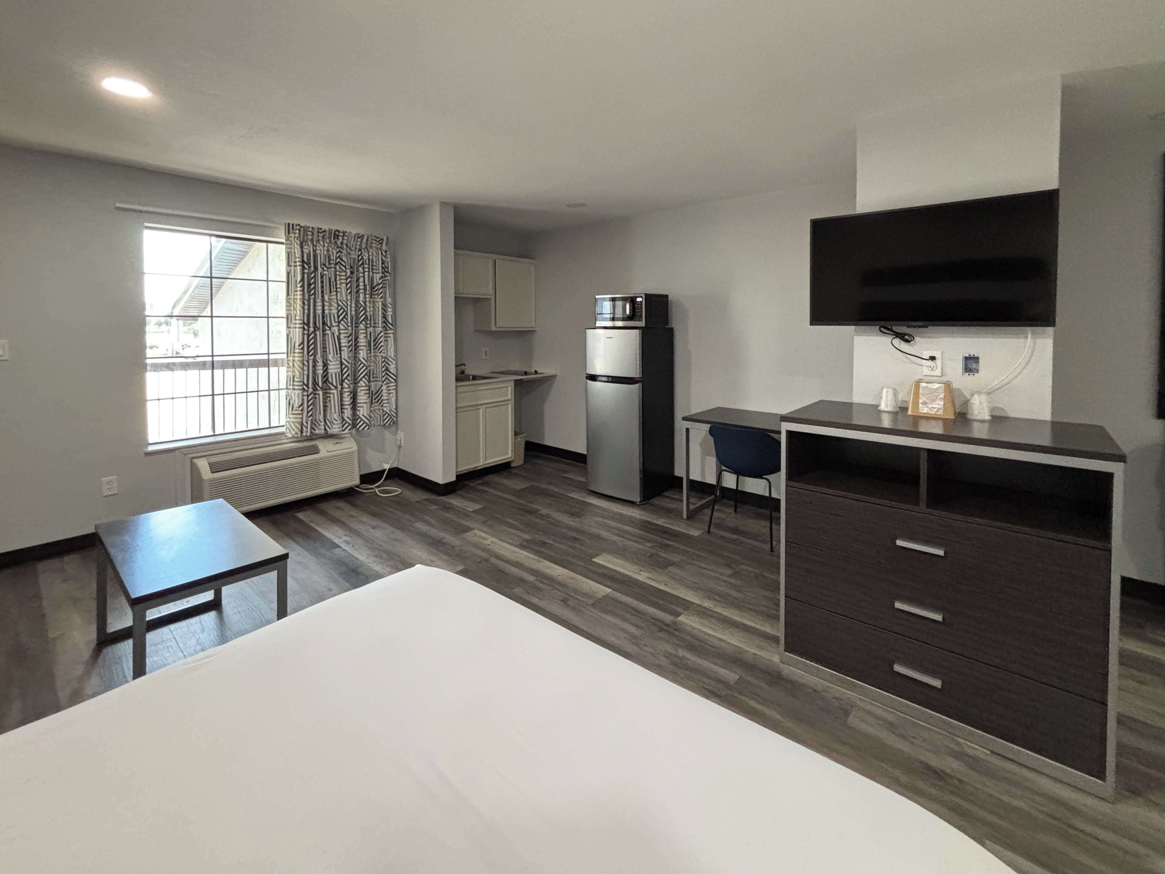 A compact hotel room with a kitchenette, a bed, a desk, and a TV.