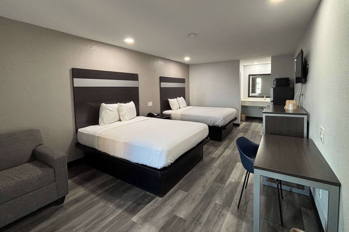 A hotel room with two beds, a desk, a chair, a sofa, and a TV.