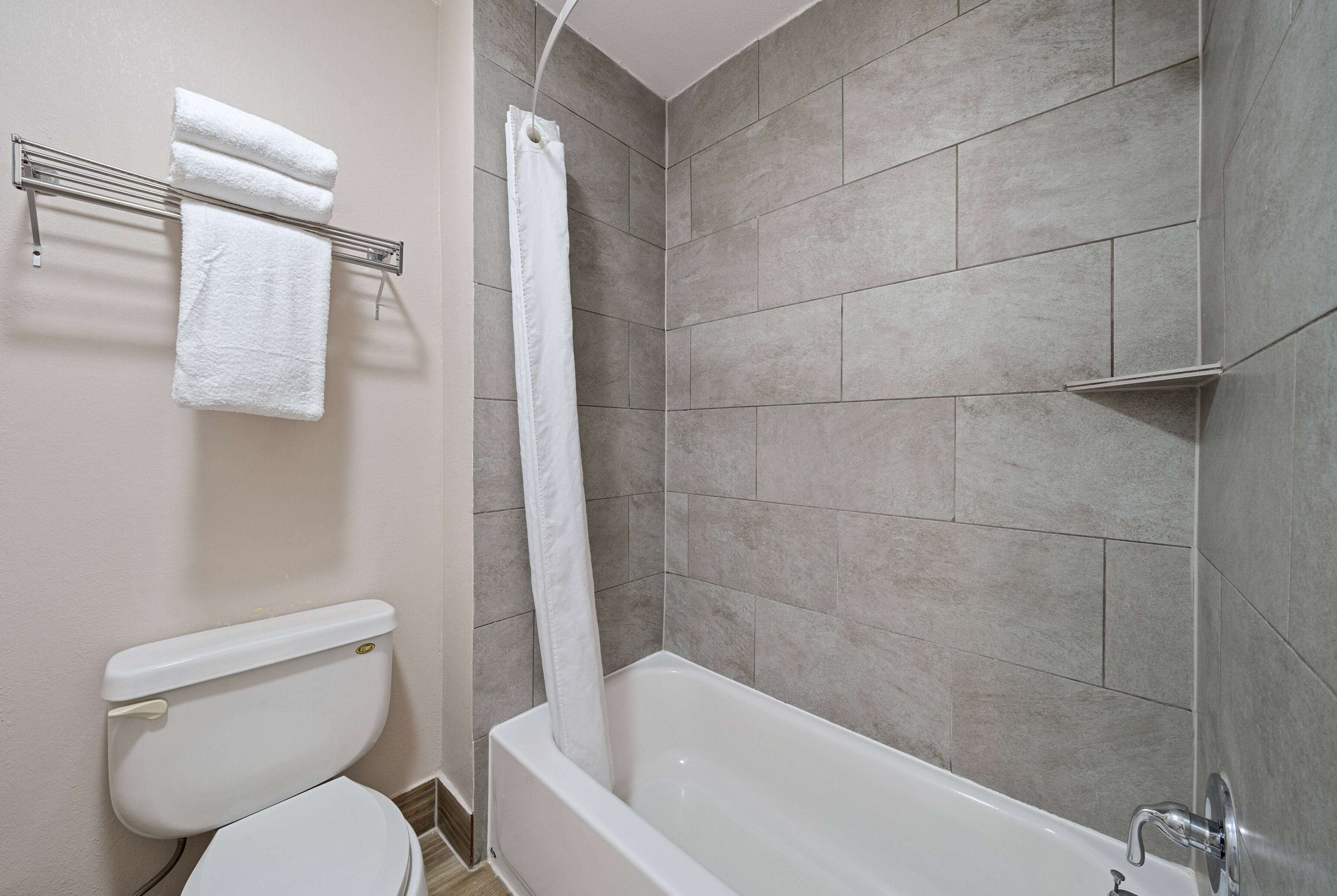 A bathroom with a bathtub, a toilet, and a towel rack with two towels.