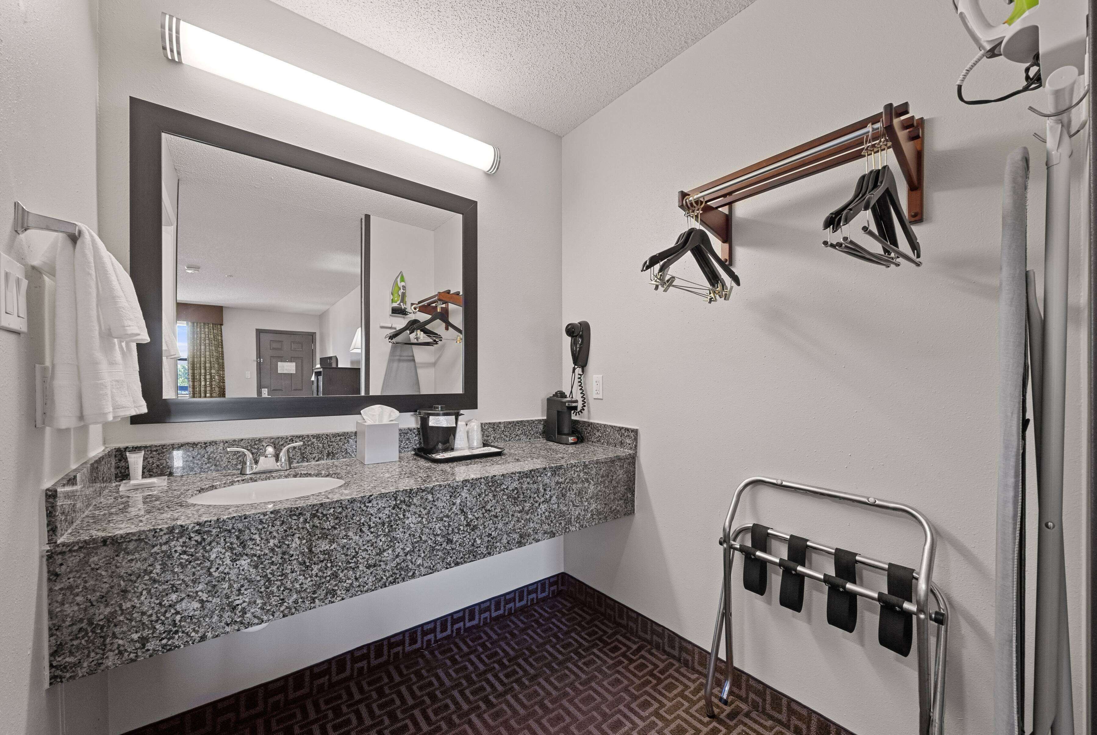 A bathroom with a granite countertop sink, a large mirror, a towel rack, and a shower area.