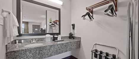 A bathroom with a granite countertop sink, a large mirror, a towel rack, and a shower area.