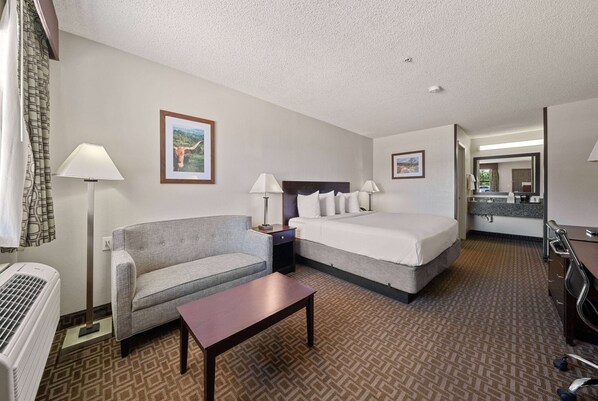 A hotel room with a bed, a sofa, a table, a lamp, and a picture on the wall.