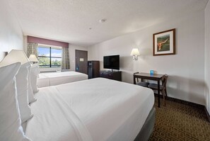 A hotel room with two beds, a desk, a TV, and a window with curtains.