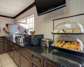 A hotel kitchen with a coffee machine, microwave, toaster, and a display case with pastries. - Econo Lodge Inn & Suites El Paso West (El Paso)