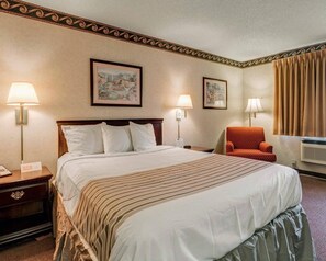 A hotel room with a large bed, two bedside lamps, a chair, and two framed pictures on the wall. - Econo Lodge Inn & Suites El Paso West (El Paso)