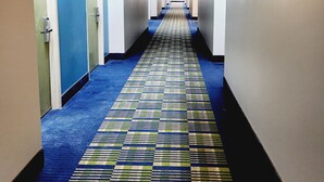 A hotel hallway with a checkered carpet, doors numbered 223 and 224, and light fixtures on the walls. - Days Inn & Suites by Wyndham Corpus Christi Central (Corpus Christi)