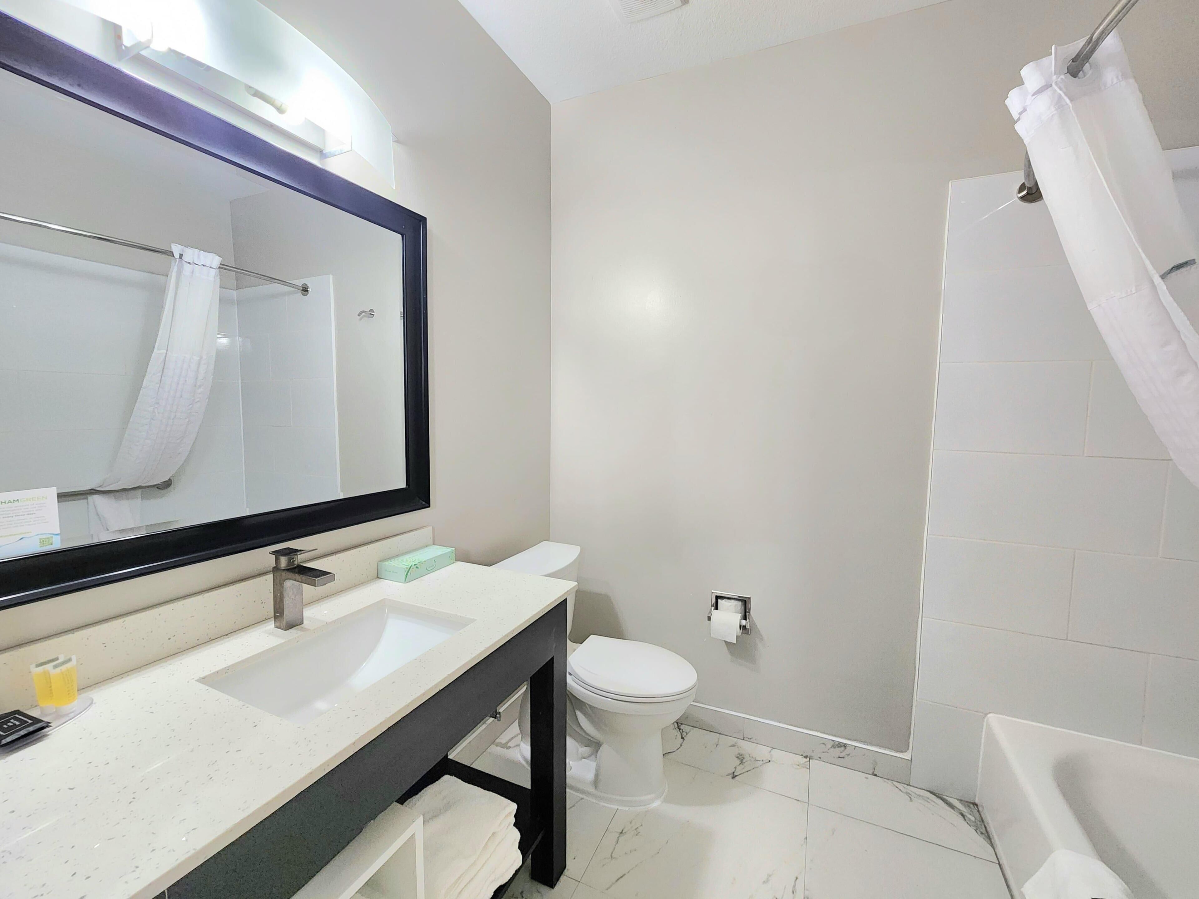 A bathroom with a white sink, mirror, toilet, and shower curtain.