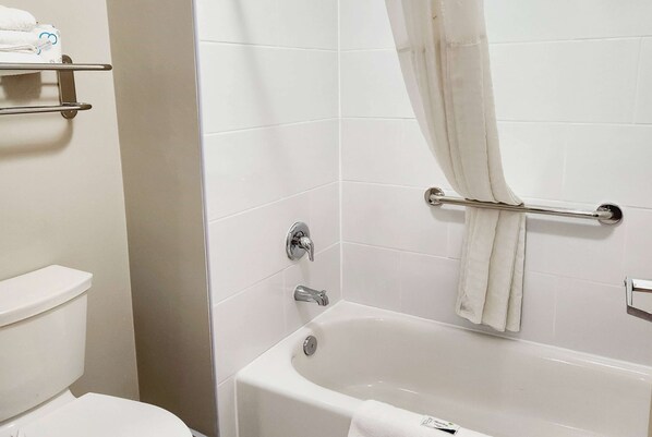 Un baño con inodoro blanco, bañera con cortina y un perchero para toallas.
