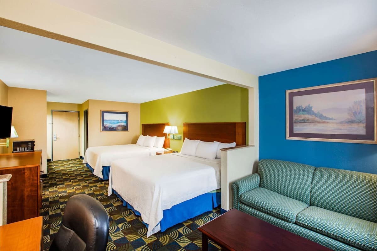 A hotel room with two beds, a desk, a sofa, and a painting on the wall.