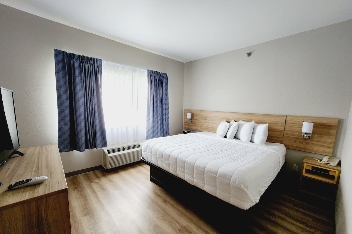 A hotel room with a bed, bedside tables, a desk, a TV, and a window with curtains.