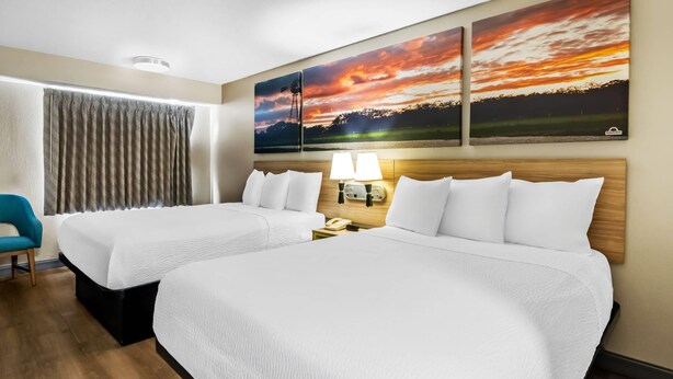 A hotel room with two beds, a desk, a chair, and a large window with curtains. - Days Inn & Suites by Wyndham DeSoto (DeSoto)