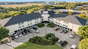 A Days Inn & Suites with a parking lot, multiple buildings, and surrounding greenery. - Days Inn & Suites by Wyndham DeSoto (DeSoto)