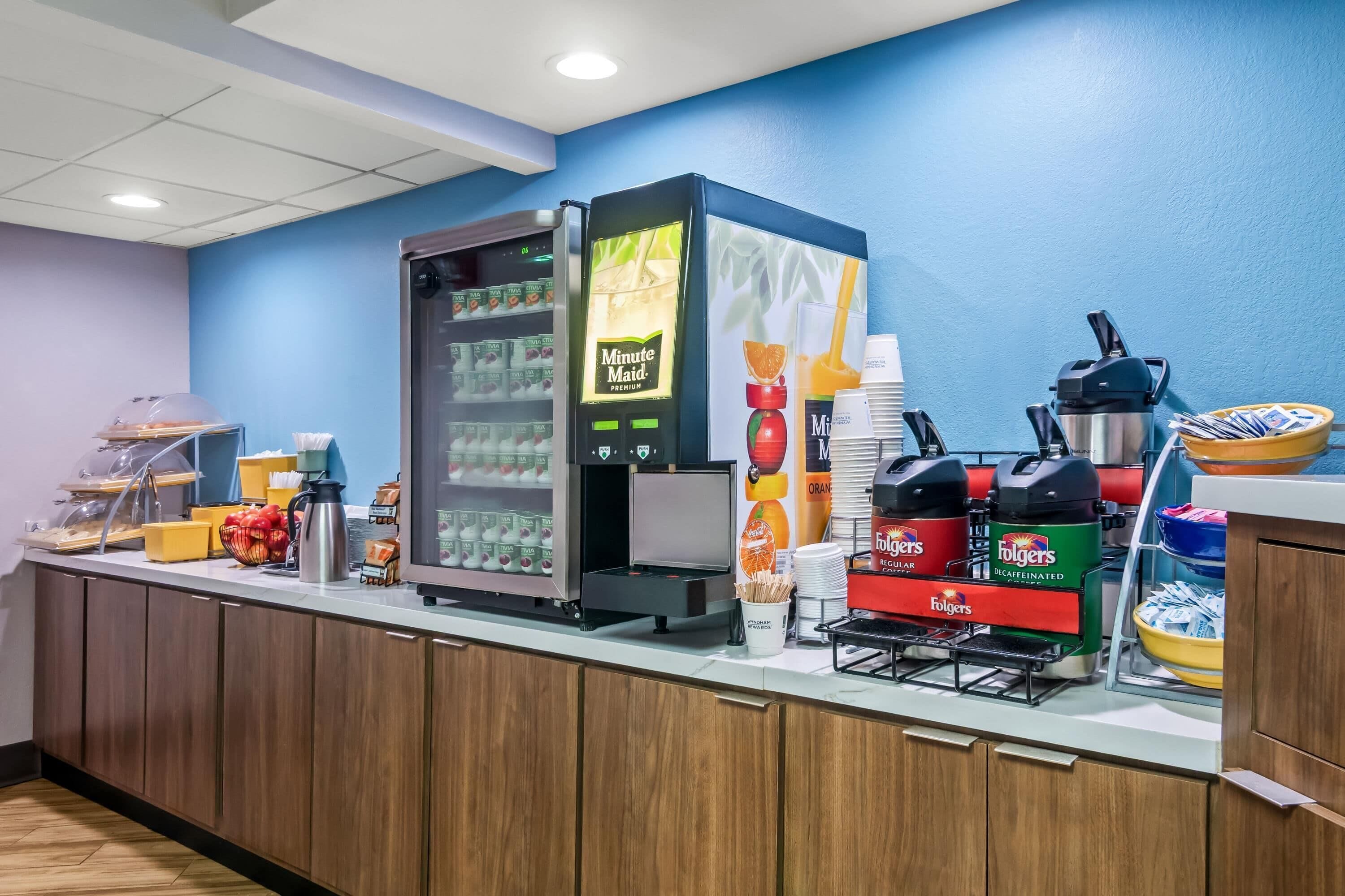 Un'area colazione a buffet con frigorifero, macchine da caffè e diverse opzioni alimentari.