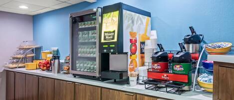 Un'area colazione a buffet con frigorifero, macchine da caffè e diverse opzioni alimentari.