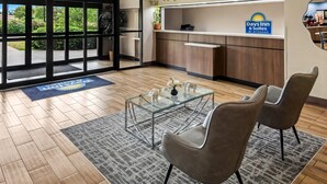 A hotel reception area with a glass coffee table, two chairs, a reception desk, and a sign for Days Inn & Suites. - Days Inn & Suites by Wyndham DeSoto (DeSoto)