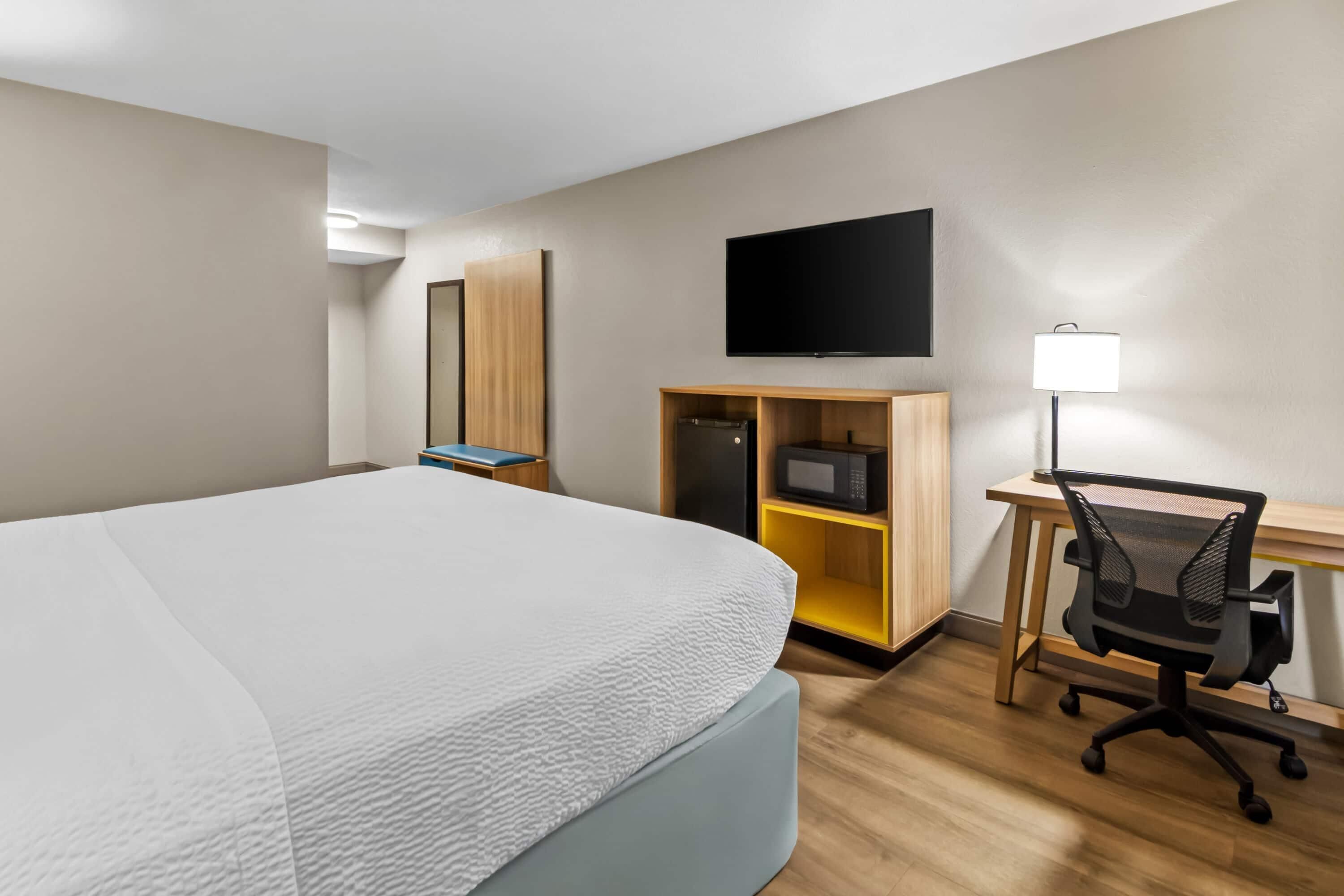 Una habitación de hotel con cama, escritorio con computadora, televisor y microondas.
