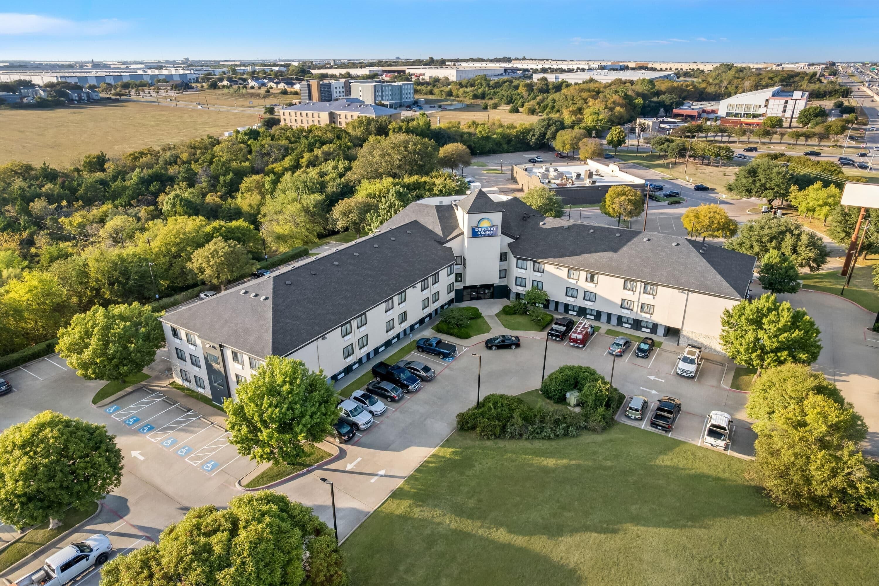 An aerial view of a hotel with multiple parking spaces, a central courtyard, and surrounding greenery.